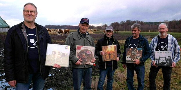 Fünf Männer stehen mit Schallplatten in der Hand auf einer Viehweide