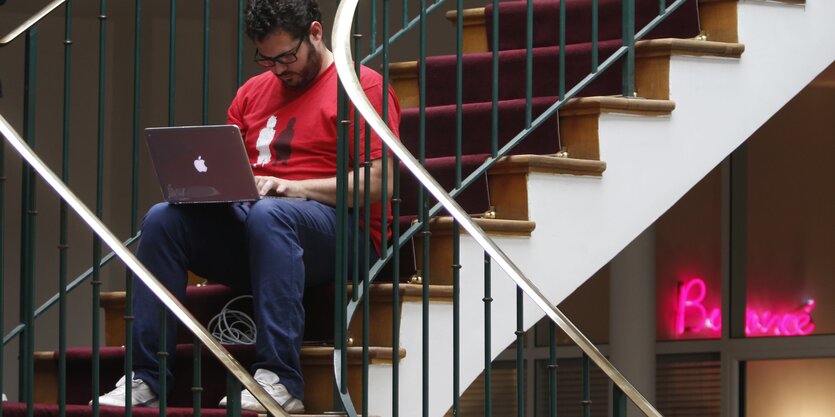 junger Mann sitzt mit Laptop auf einer Treppe