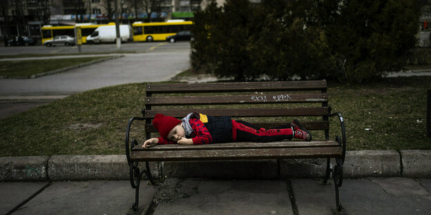 Ein Junge ruht sich liegend auf einer Parkbank aus