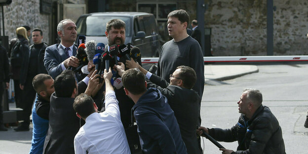 Viele Reporter knien mit ihren Mikrofonen vor einemm Mann