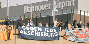 Aktivist*innen am Flughafen Hannover mit einem Transparent, auf dem steht: "Gegen jede Abschiebung"