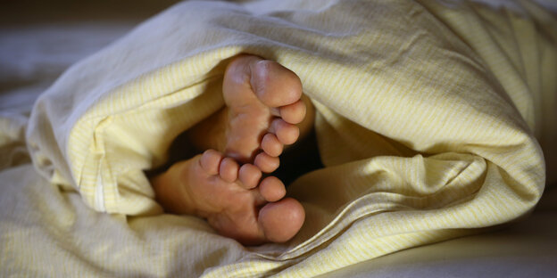 Die Füße einer Frau ragen unter einer Bettdecke hervor.
