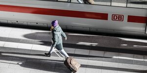 Eine Frau geht mit einem Rollkoffer auf dem Bahnsteig neben einem ICE