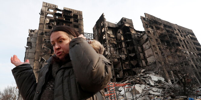 Eine Frau läuft mit ratlosem Gesichtsausdruck vor einem zerbombten Haus entlang