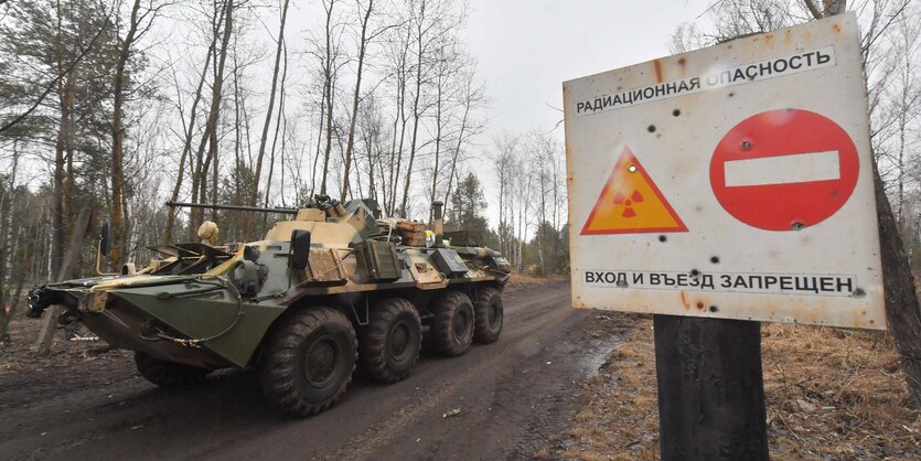 Ein Radpanzer steht hinter einem Schild, auf dem ein Stopp-Symbol und ein Strahlungssymbol zu sehen sind.