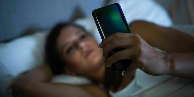 Eine Frau liegt im Bett und starrt auf ihr Handy