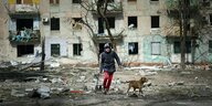 Ein Mann geht mit seinem Hund durch Trümmer in einem zerstörten Wohngebiet