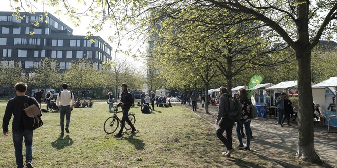 Menschen flanieren durch den sonnigen Besselpark, die Kastanien knospen, im Hintergrund erhebt sich der taz neubau