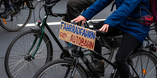 Radfahrer mit einem Schild mit der Aufschrift „„Fahrradfahr’n“ statt Autobahn“