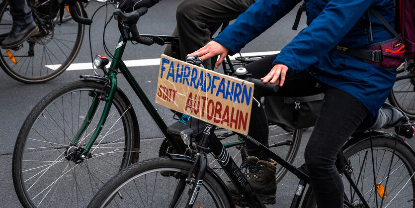 Radfahrer mit einem Schild mit der Aufschrift „„Fahrradfahr’n“ statt Autobahn“