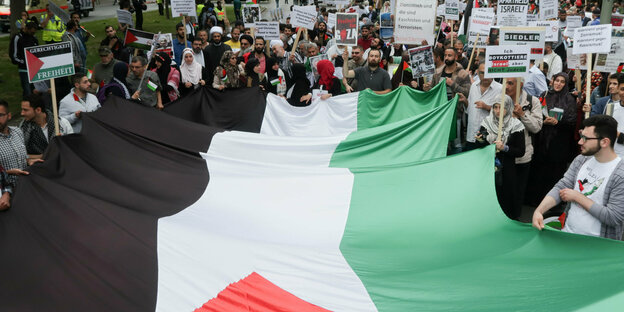Menschen stehen auf einer Demo hinter einer palästinensischen Fahne
