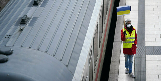 Ein Helfer des Arbeiter-Samariter-Bundes (ASB) hält ein Schild mit der Flagge der Ukraine auf einem Bahnsteig hoch