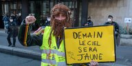 Ein Mann mit Perücke, falschen Bart und gelber Warnweste hält ein Protestplakat hoch