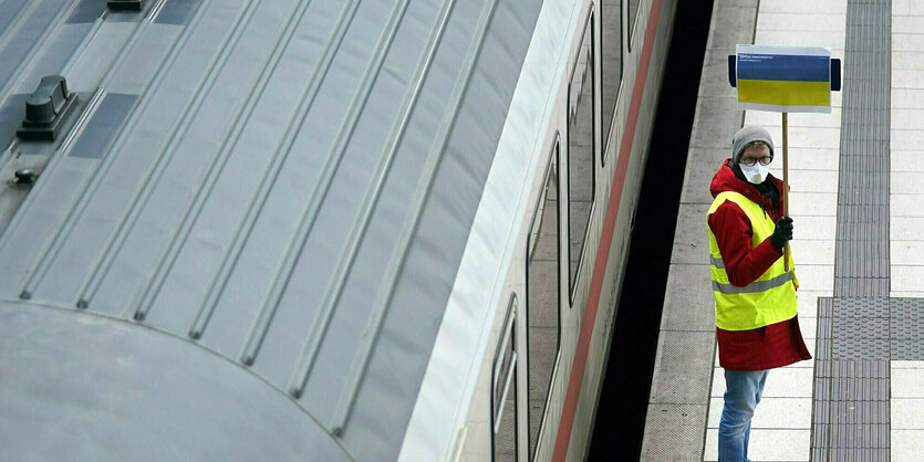 Ein Helfer hält ein Schild mit der Flagge der Ukraine auf einem Bahnsteig im Hauptbahnhof hoch.