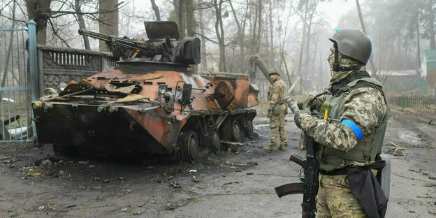 Ukrainische Soldaten untersuchen ein zerstörtes Militärfahrzeug
