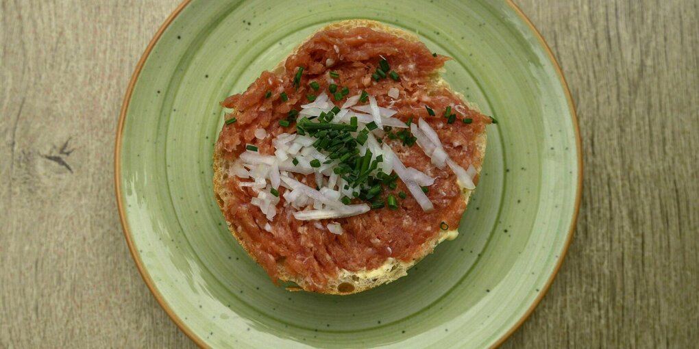 Ein Mettbrötchen mit Zwiebeln liegt auf einem grünen Teller