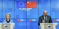 Zwei Menschen stehen an Rednerpulten vor einem blauen Greenscreen, über ihren Köpfen wird die chinesische und die EU-Flagge angezeigt.