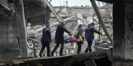 Ukrainische Rettungskräfte tragen eine ältere Frau unter einer zerstörten Brücke