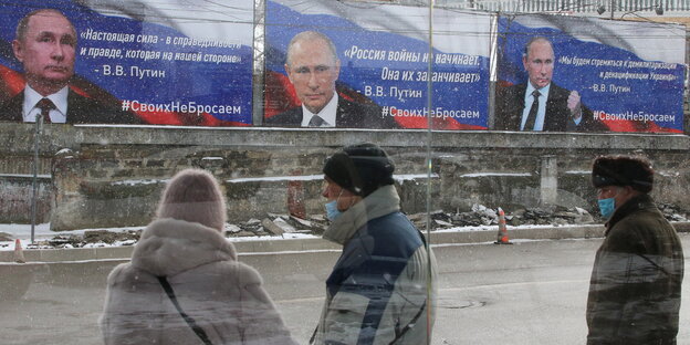 Menschen stehen vor Plakaten, auf denen Putin groß zu sehen ist