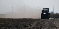 Traktor auf Acker in großer Staubwolke, im Hintergrund Windräder.