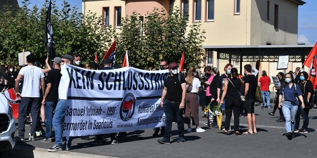 Eine Menschenmenge auf einer Starße in Saarlouis, einige Menschen halten ein Transparent mit der Aufschtrift "Kein Schlussstrich"