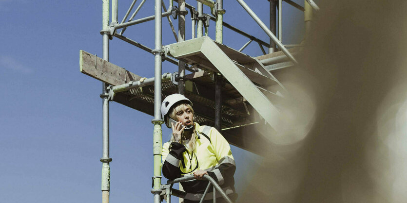 Eine Bauarbeiterin steht auf einem Baugerüst und telefoniert