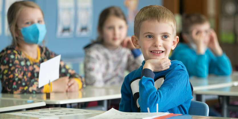 Vier Kinder in einem Klassenraum. Nur ein Mädchen links trägt eine Maske