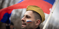Eine Person mit Soldatenmütze und russischer Fahne