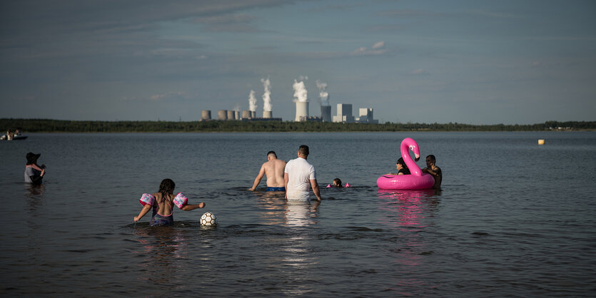 Menschen baden vor der Kulisse eines Kohlekraftwerks