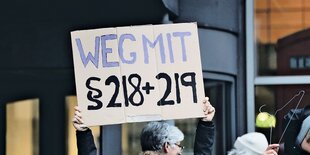 Eine Person hält ein Schild mit der Aufschrift "Weg mit Paragraph 218 und 219" in die Höhe.