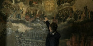 Ein Mann fährt mit seiner Hand über ein sehr altes Wandgemälde