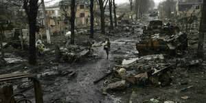 Eine Straße mit ausgebrannten Militärfahrzeugen, ein Mensch geht durch die Trümmer