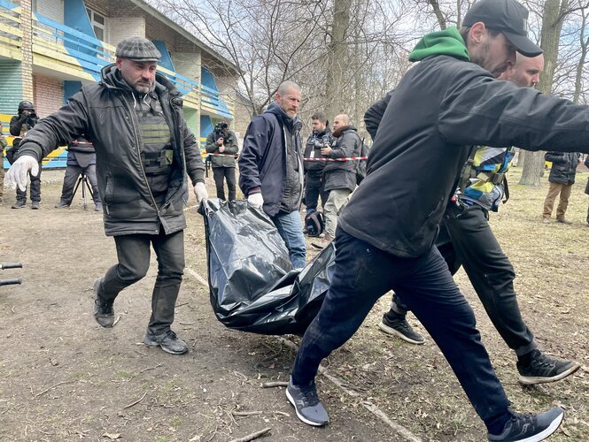 Mehrere Männer transportieren eine Leich in einem schwarzen Sack