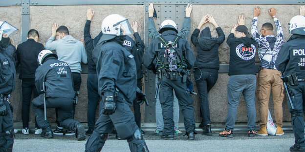Junge Menschen müssen mit dem Gesicht zu einer Mauer stehen und werden von Polizisten festgehalten