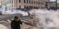 Ein Mann presst sich inmitten von Tränengasschwaden seine Maske vor den Mund