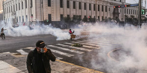 Ein Mann presst sich inmitten von Tränengasschwaden seine Maske vor den Mund
