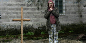 Eine Frau trauert an einem Grab mit provisorischen Holzkreuz