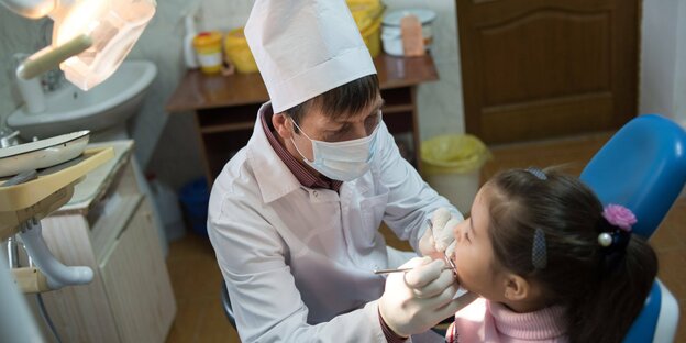 Zahnarzt im weißen Kittel untersucht ein kleines Mädchen