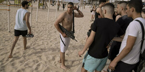 Ein Mann in Badehose un dmit einem Maschinengewehr am Strand