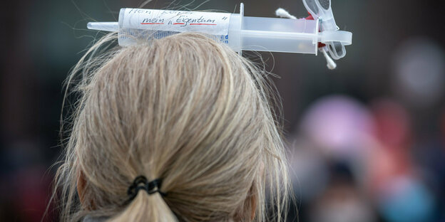 Eine Frau trägt eine gebastelte Spritze auf dem Kopf. Auf der Spritze steht: "Mein Körper, mein Eigentum"