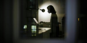 Die Silhouette einer Frau, die am Schreibtisch sitzt, ist durch ein Fenster zu sehen