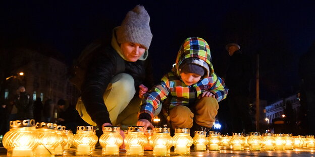 Eine Frau und ein kleiner Junge knien vor brennenden Kerzen auf der Erde