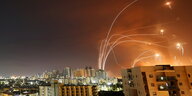 Leuchtstreifen von Raketenbeschuss an einem Abendhimmel über Hochhäusern