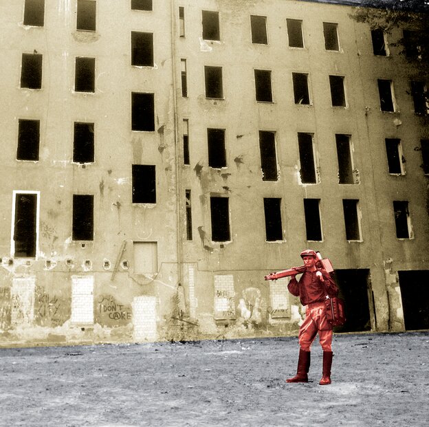 Gerd Conradt steht verkleidet als der sowjetische Regisseur Dsiga Wertow als rote Figur vor blasser Fassade.