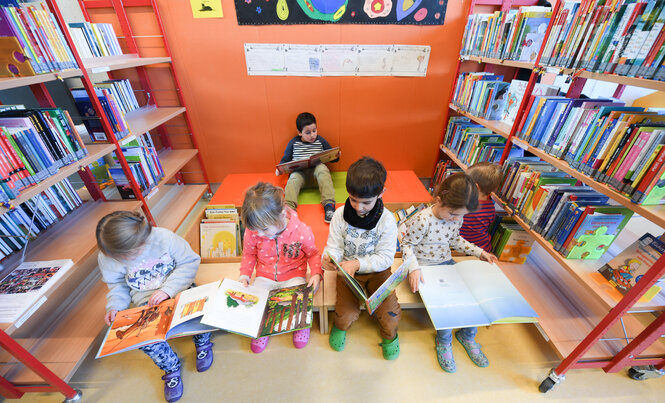 Eine Bibliothek und lesende Kinder mit Büchern auf dem Schoß