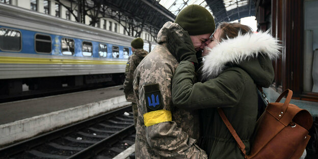 Ein Soldat und eine Frau umarmen sich auf einem Bahnsteig