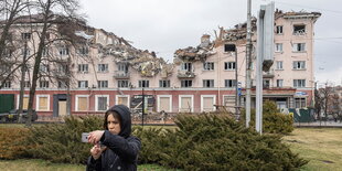 Eine Frau macht ein Selfie vor einem zerstörten Gebäude