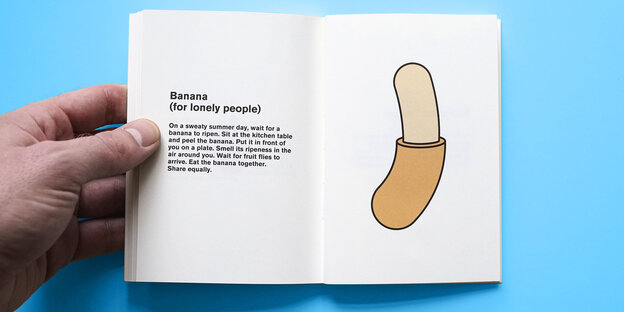 Eine Hand schlägt ein kleines Buch auf, darin eine gezeichnete Banane und ein wenig Text