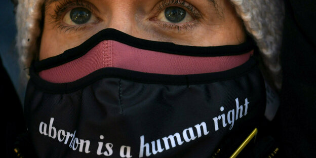 Frau mit schwarzer Atemschutzmaske, auf der in Englisch steht: Abreibung ist ein Menschenrecht.