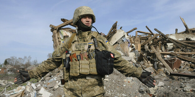Ein ukrainischer Soldat steht nach einem Granatenbeschuss vor einem Trümmerhaufen und streckt die Arme aus